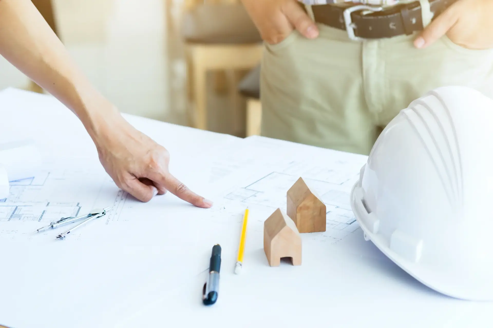 Architect pointing at blueprints next to a hardhat and small wooden house models by Custom Home Builders in Greenville SC.