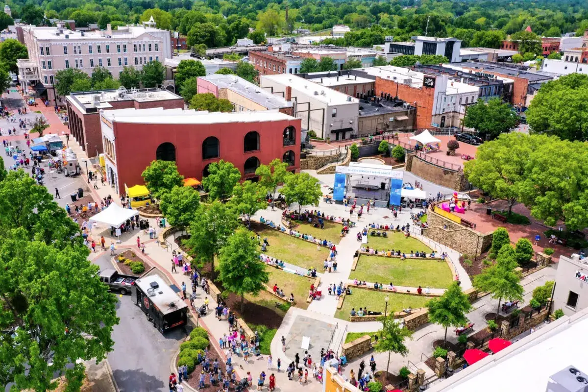 Aerial view of a city park with people gathered near a stage, supported by custom home builders in Anderson SC.