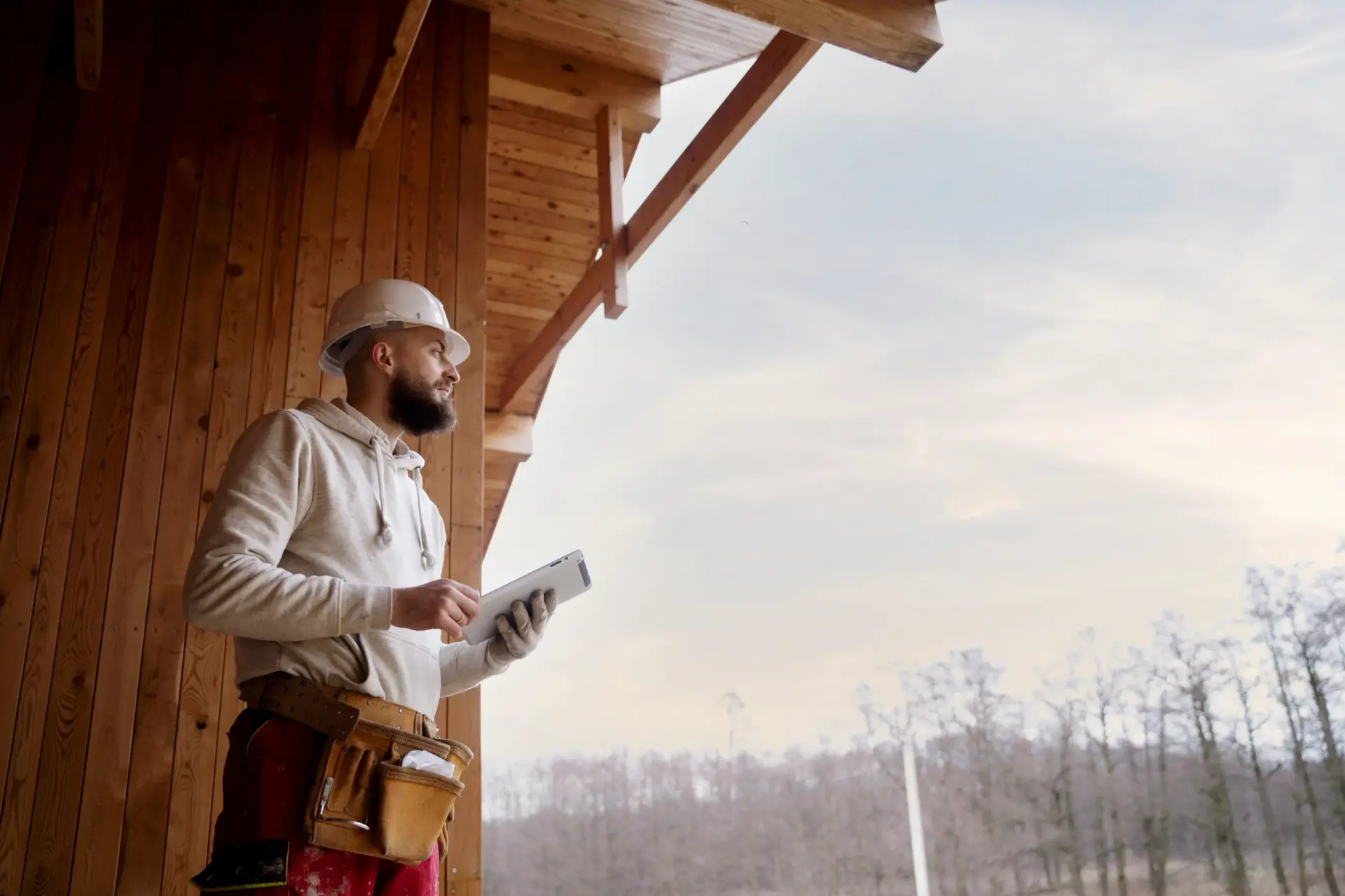 Contractor in a hard hat using a tablet at a wooden structure site managed by Custom Home Builders in Spartanburg SC.