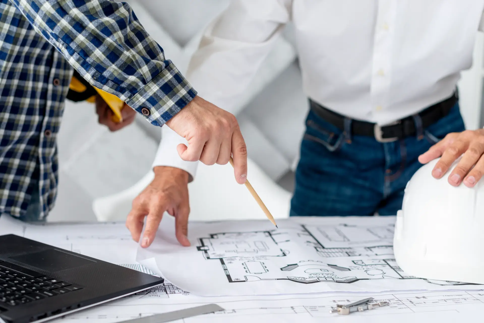 Expert pointing at house floor plans during Construction Consulting in South Carolina with a laptop and white hard hat.