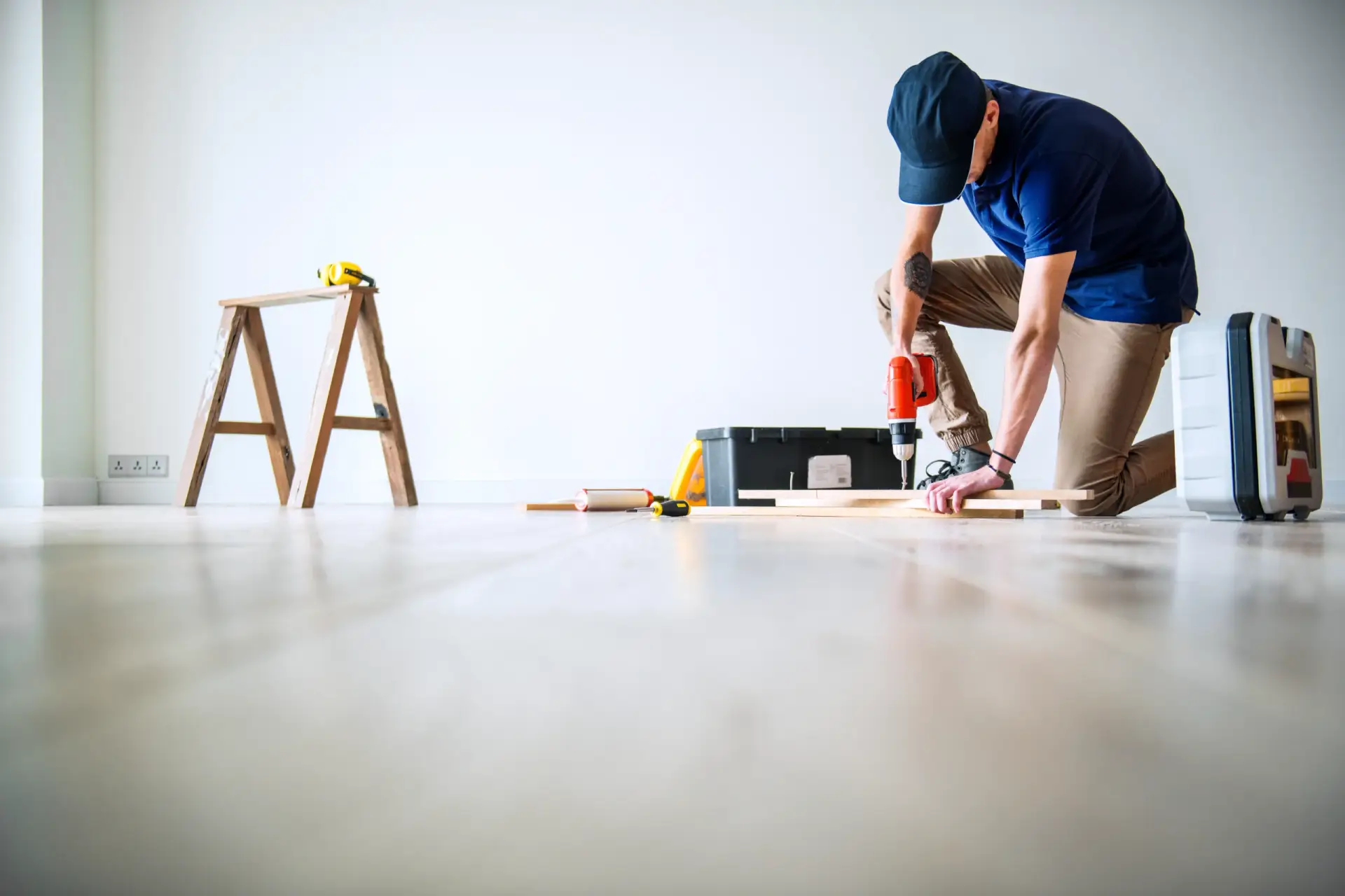 A contractor kneeling on a light wood floor using a drill for Home Remodeling in South Carolina.
