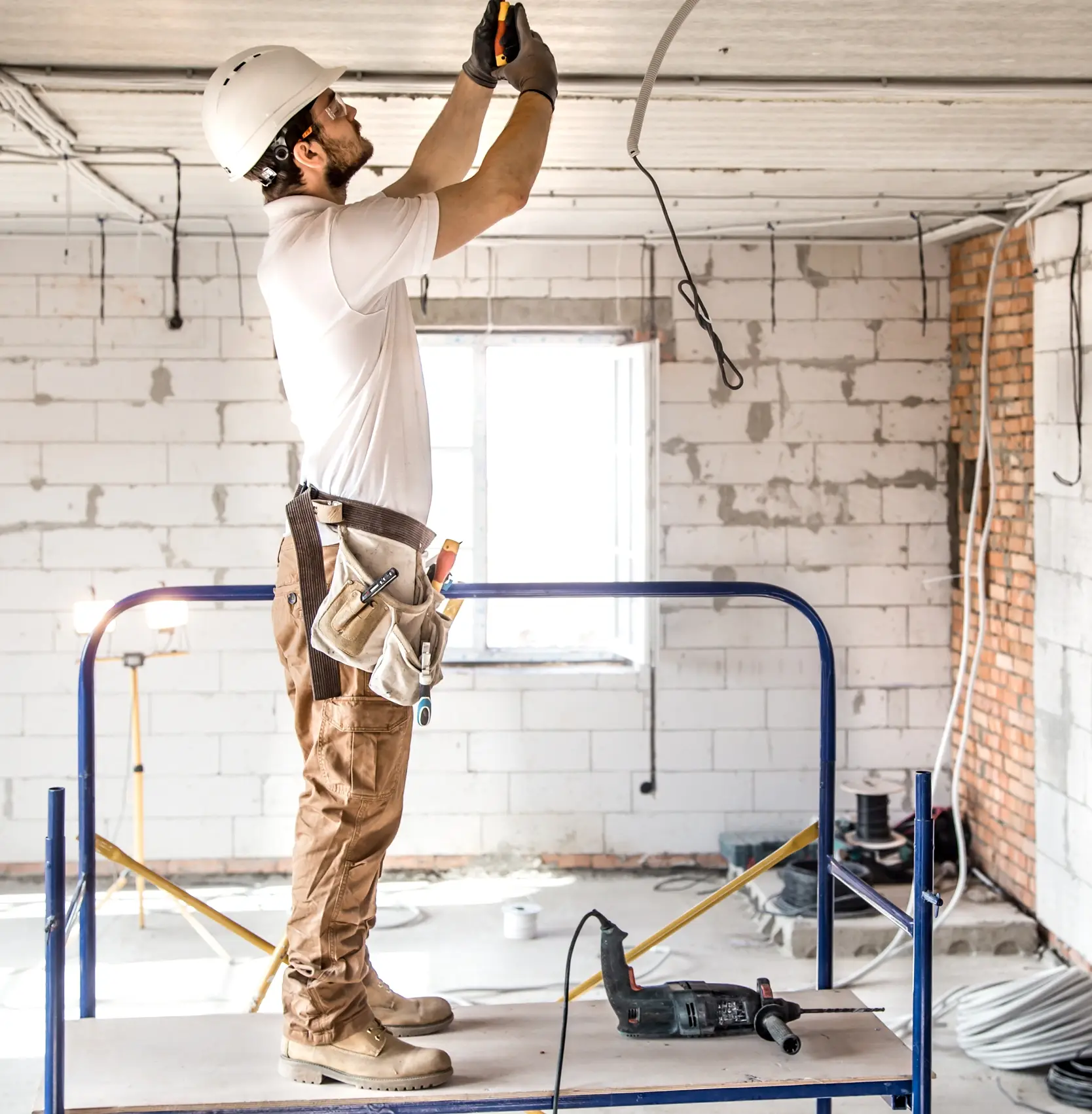 Expert electrician on scaffolding installing a classic chandelier, a process managed by Custom Home Builders in South Carolina.