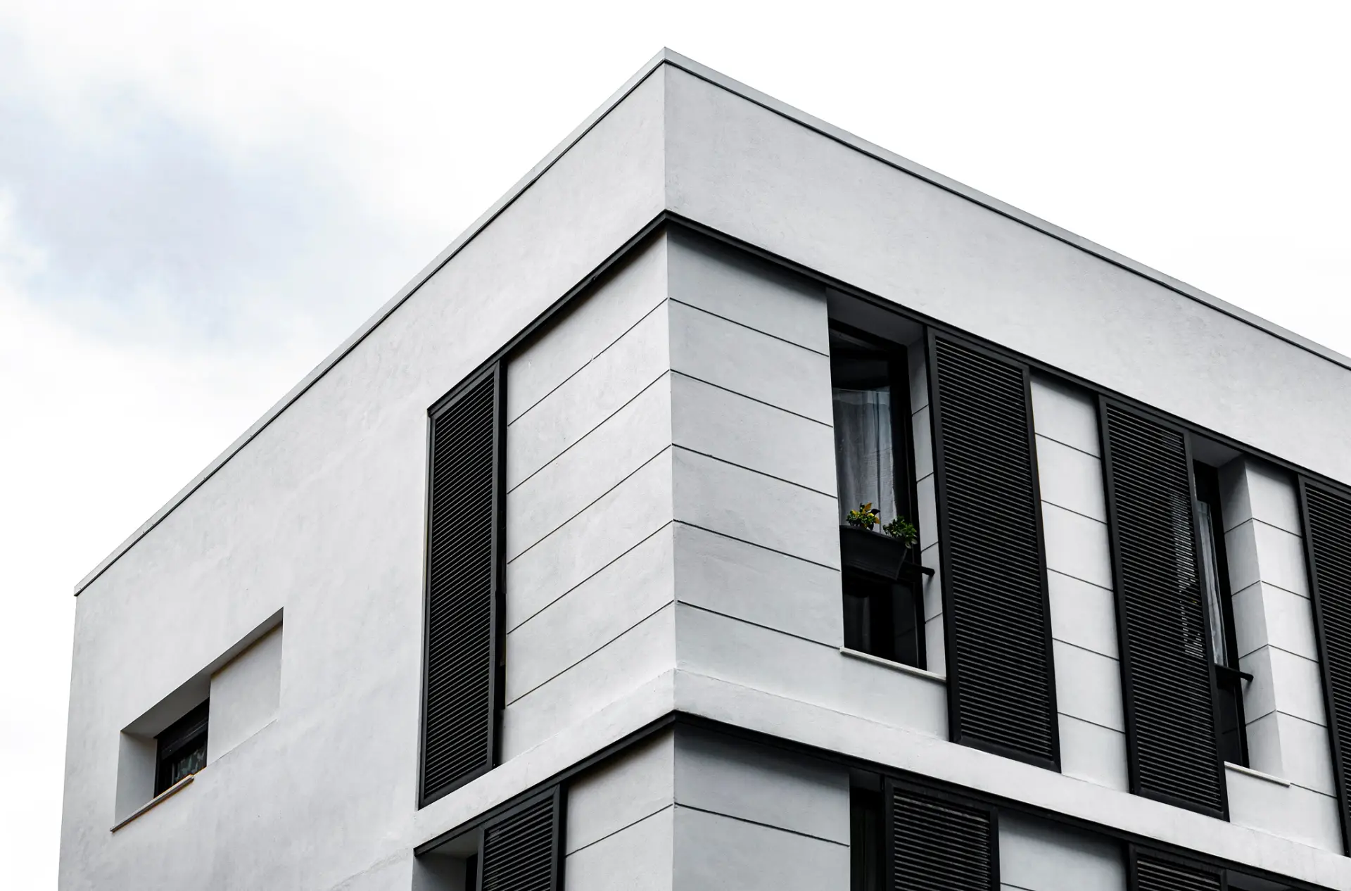 Low angle view of a modern white building with black louvered shutters, a style Custom Home Builders in South Carolina can replicate.