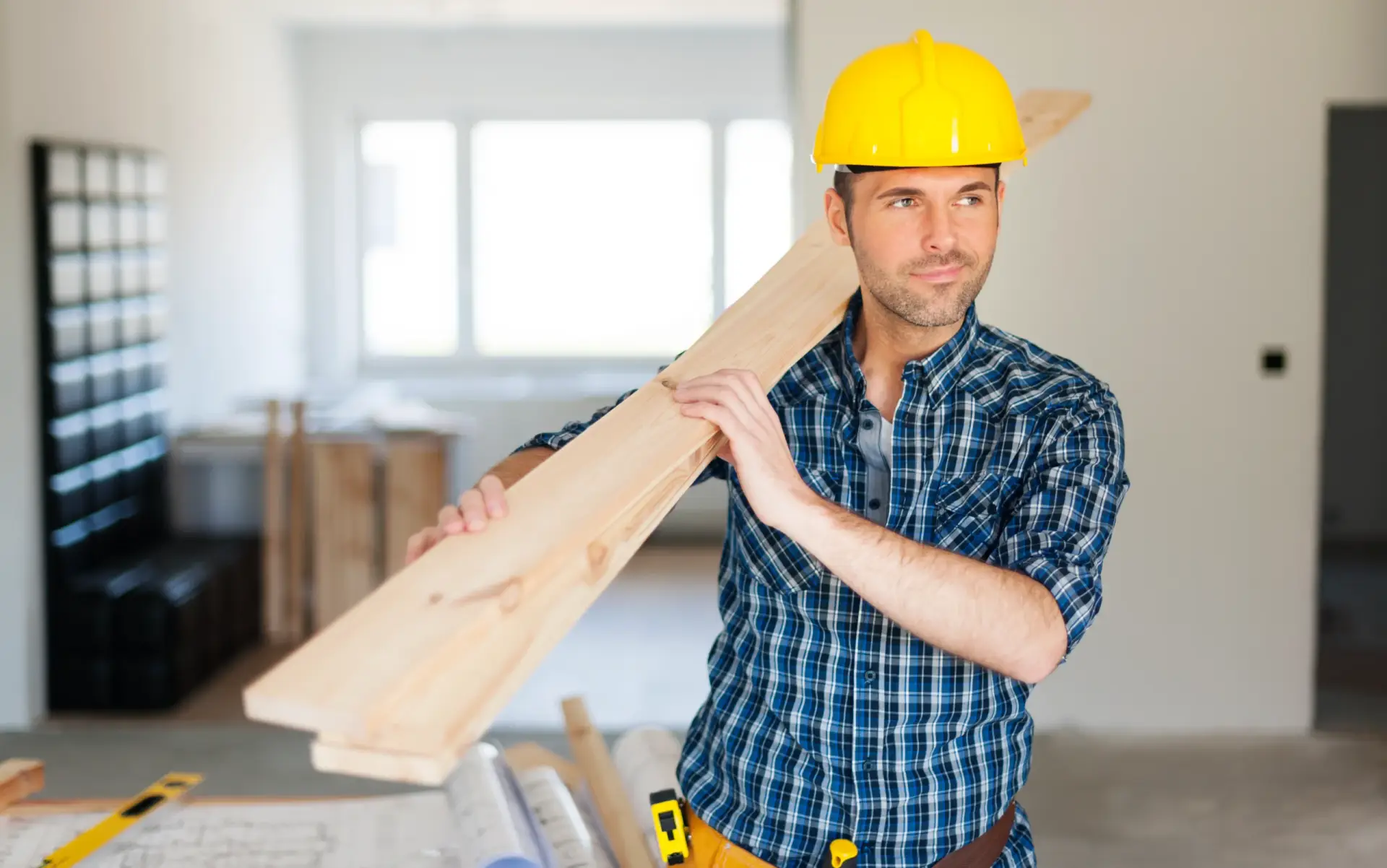 A man in a yellow hard hat carrying wooden planks at a site managed by custom home builders in Easley SC.
