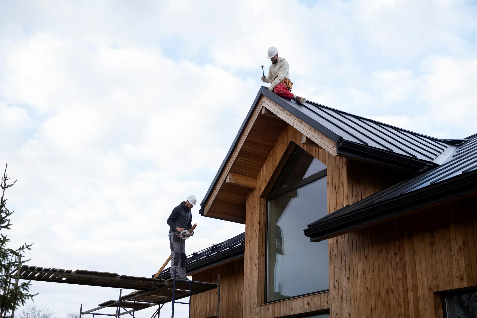 Roofing contractors from Custom Home Builders in South Carolina install a black metal roof on a modern timber house.