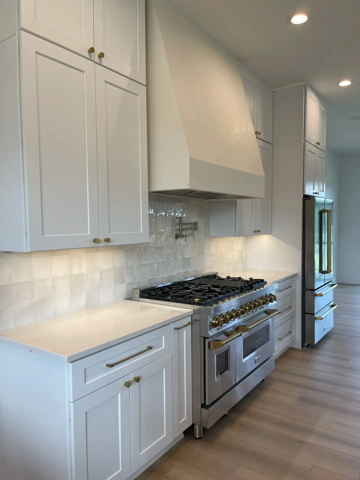 White shaker cabinets, a micro cement hood, and a gas range with gold knobs in a Modern Farmhouse Craftsma kitchen.