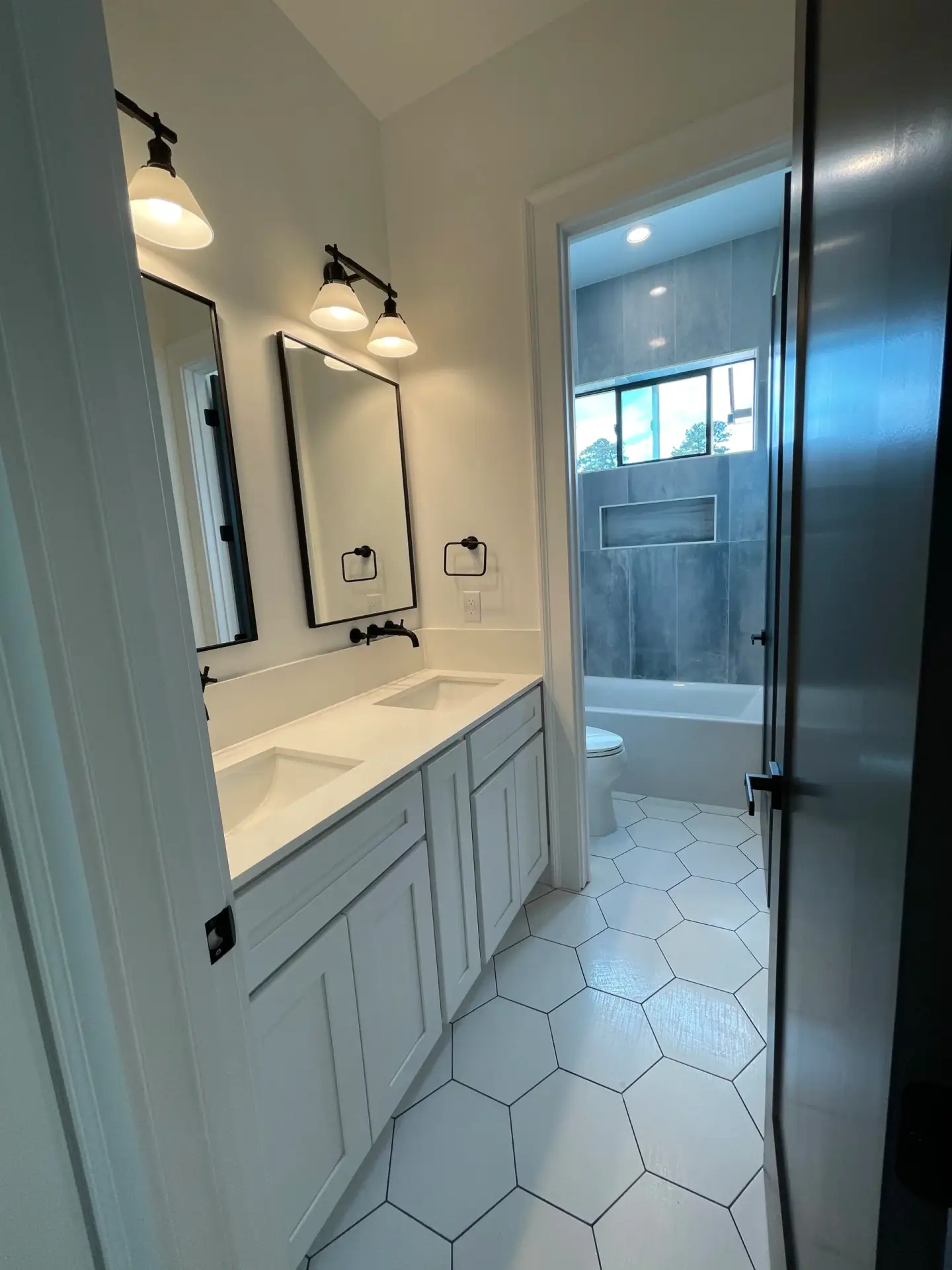 A double vanity bathroom with white hexagon floor tiles and matte black fixtures in a Modern Farmhouse Craftsma.