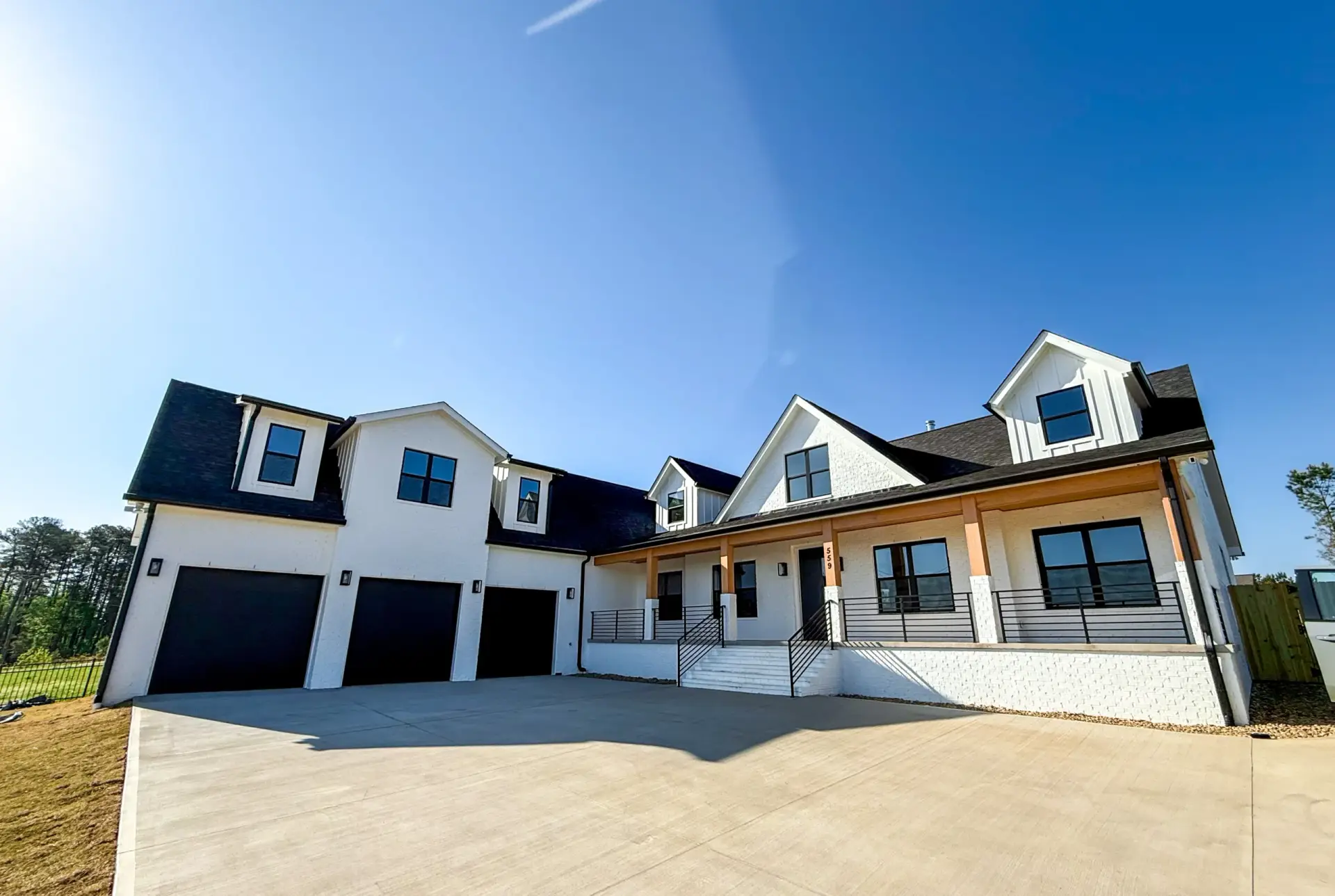 A white Modern Farmhouse Craftsman exterior with black trim, a three-car garage, and a large concrete driveway.