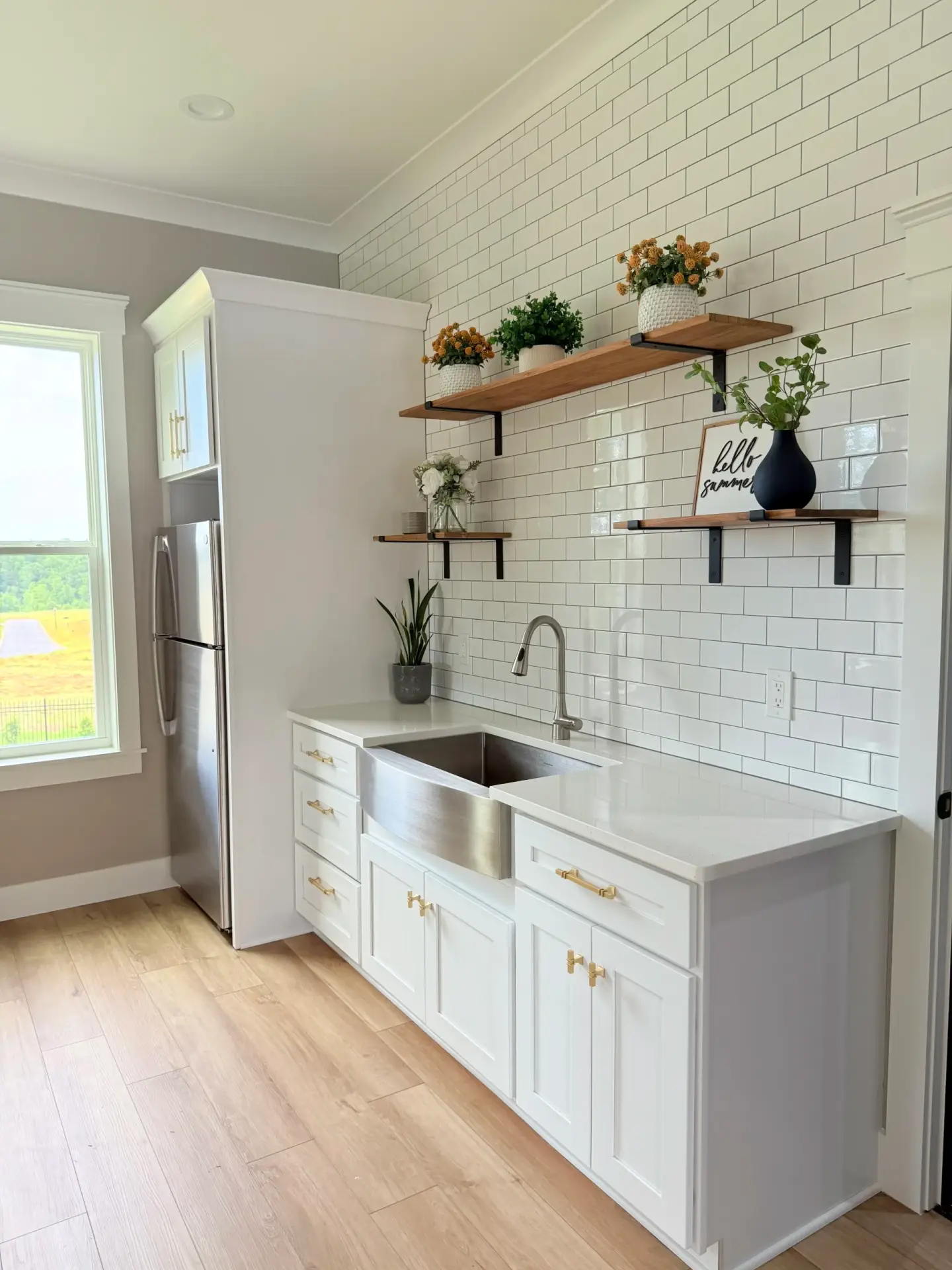 White kitchen cabinets, subway tile backsplash, stainless steel farmhouse sink, and wooden shelves in a Custom Luxury Pool House.