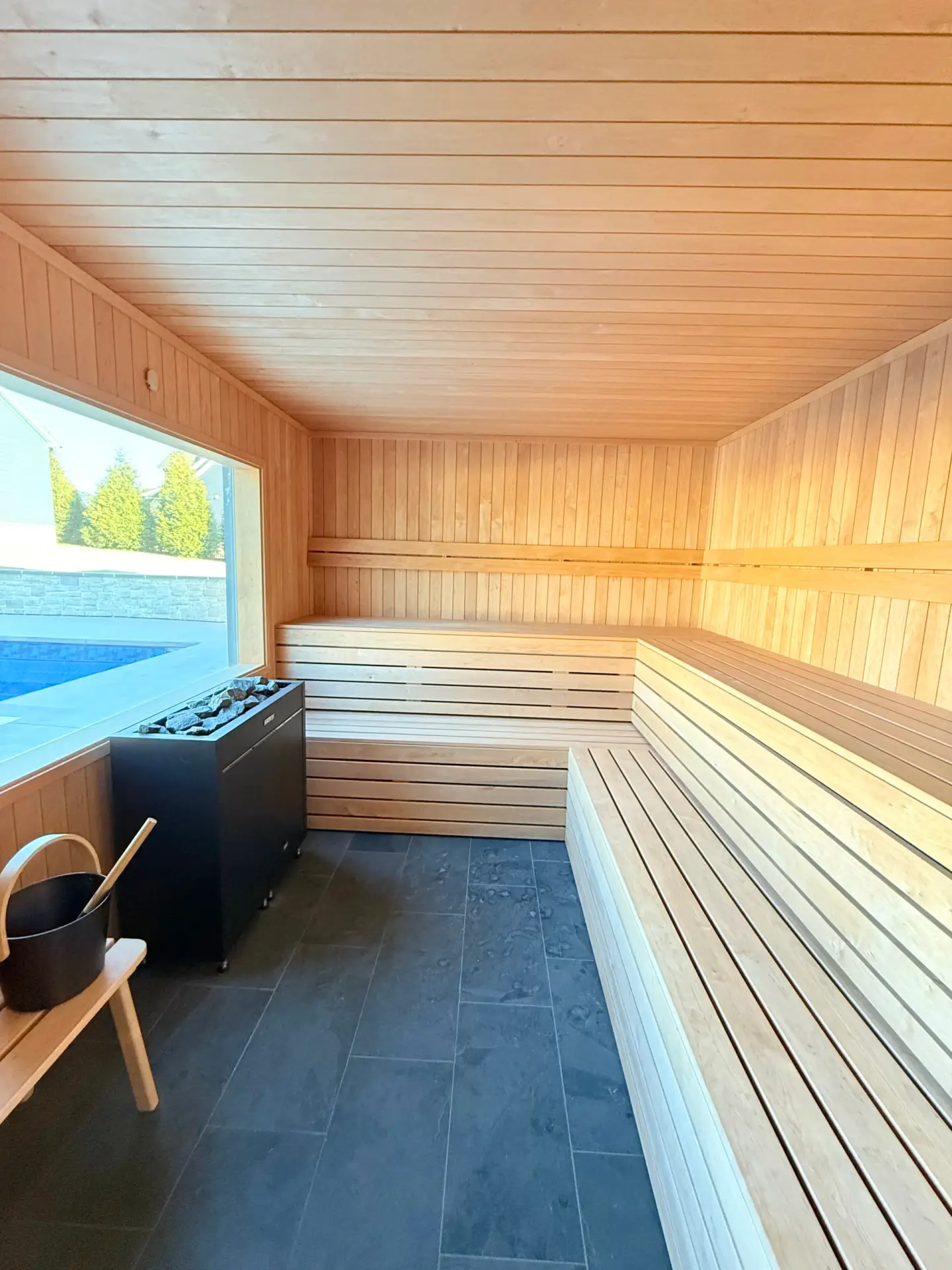 Sauna with black alder wood benches, slate tile floor, electric heater, and a pool view inside a Custom Luxury Pool House.