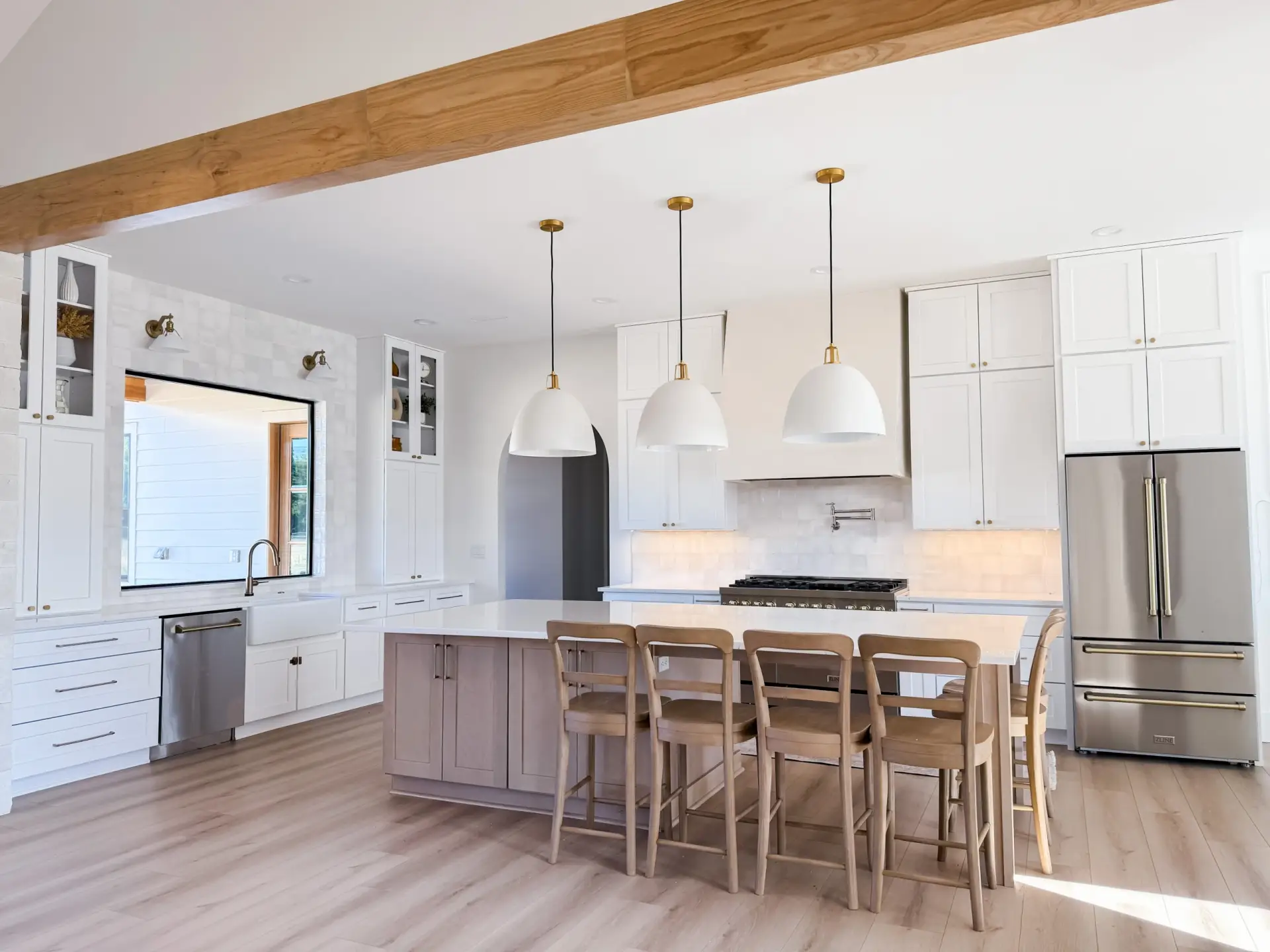 A large white Modern Farmhouse Craftsma kitchen with a center island, wooden barstools, and dome pendant lights.