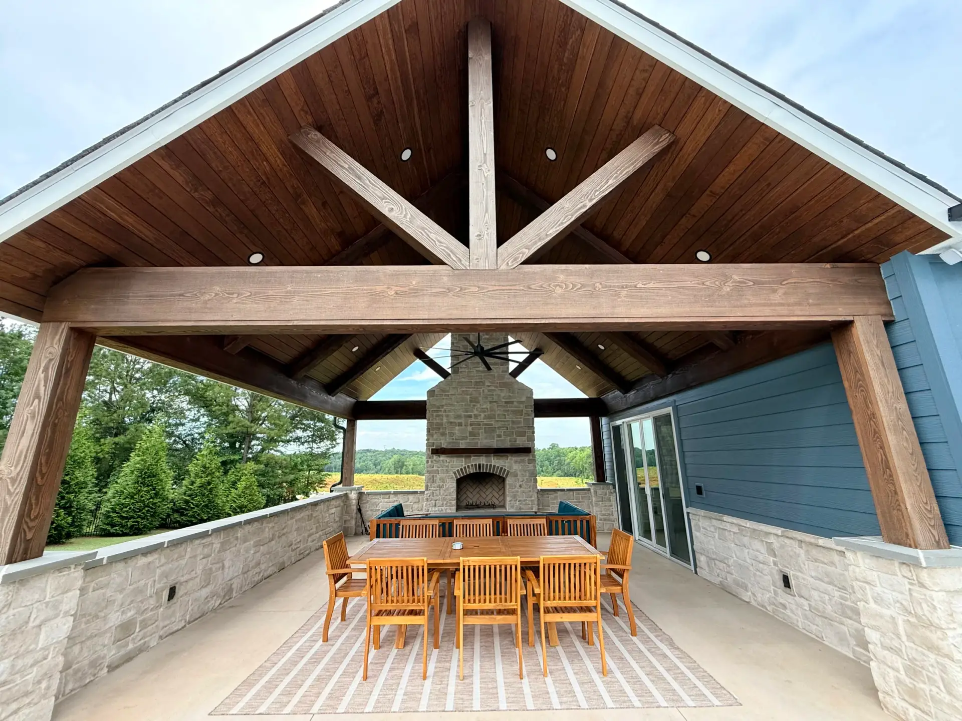 Wooden pavilion with a stone wood-burning fireplace and dining set at a Custom Luxury Pool House.